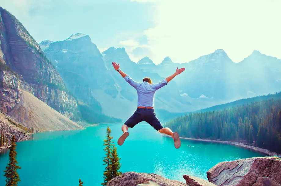 a person jumping in the air before a blue lake and mountains